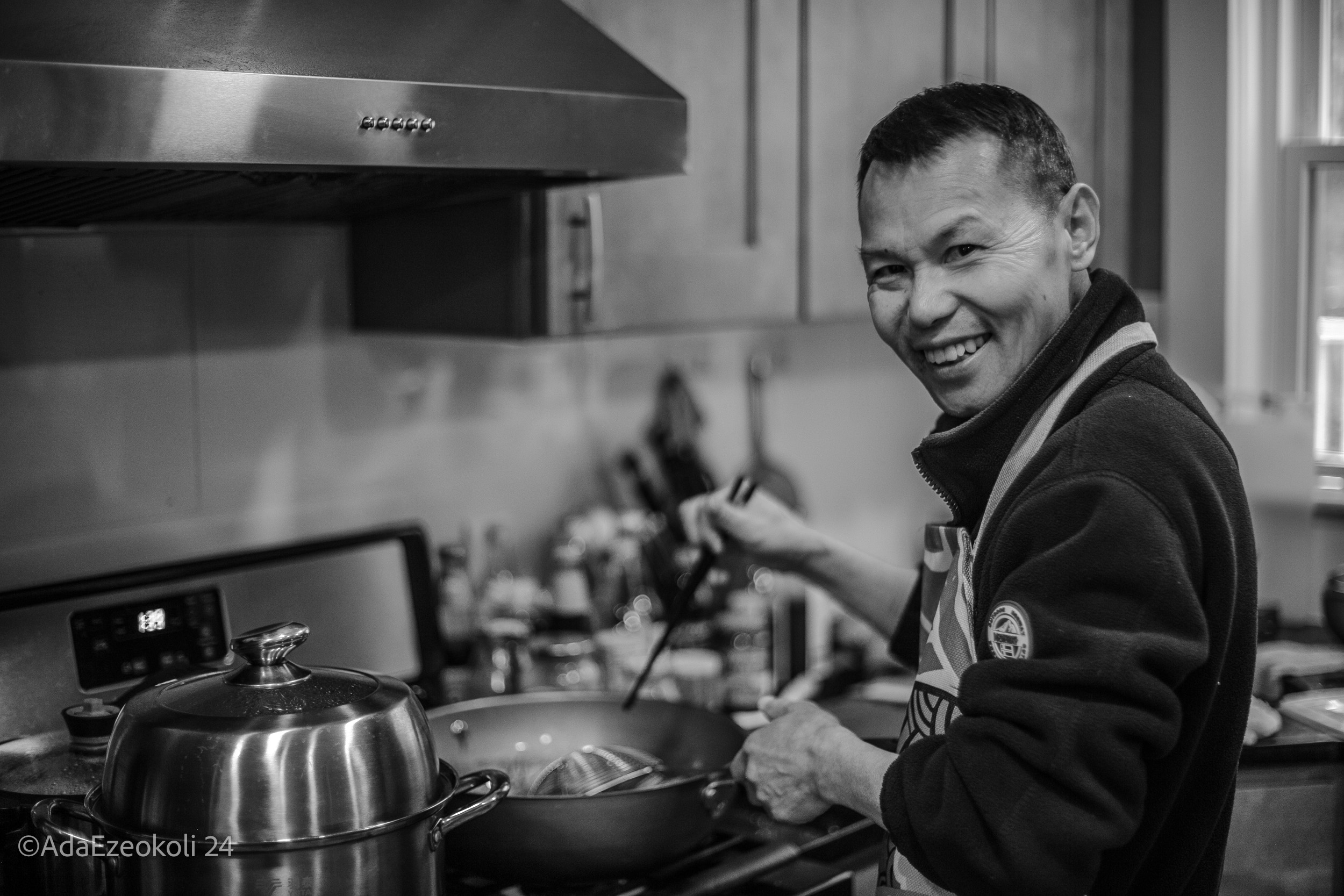 An asian man cooking in a kitchen and smiling
