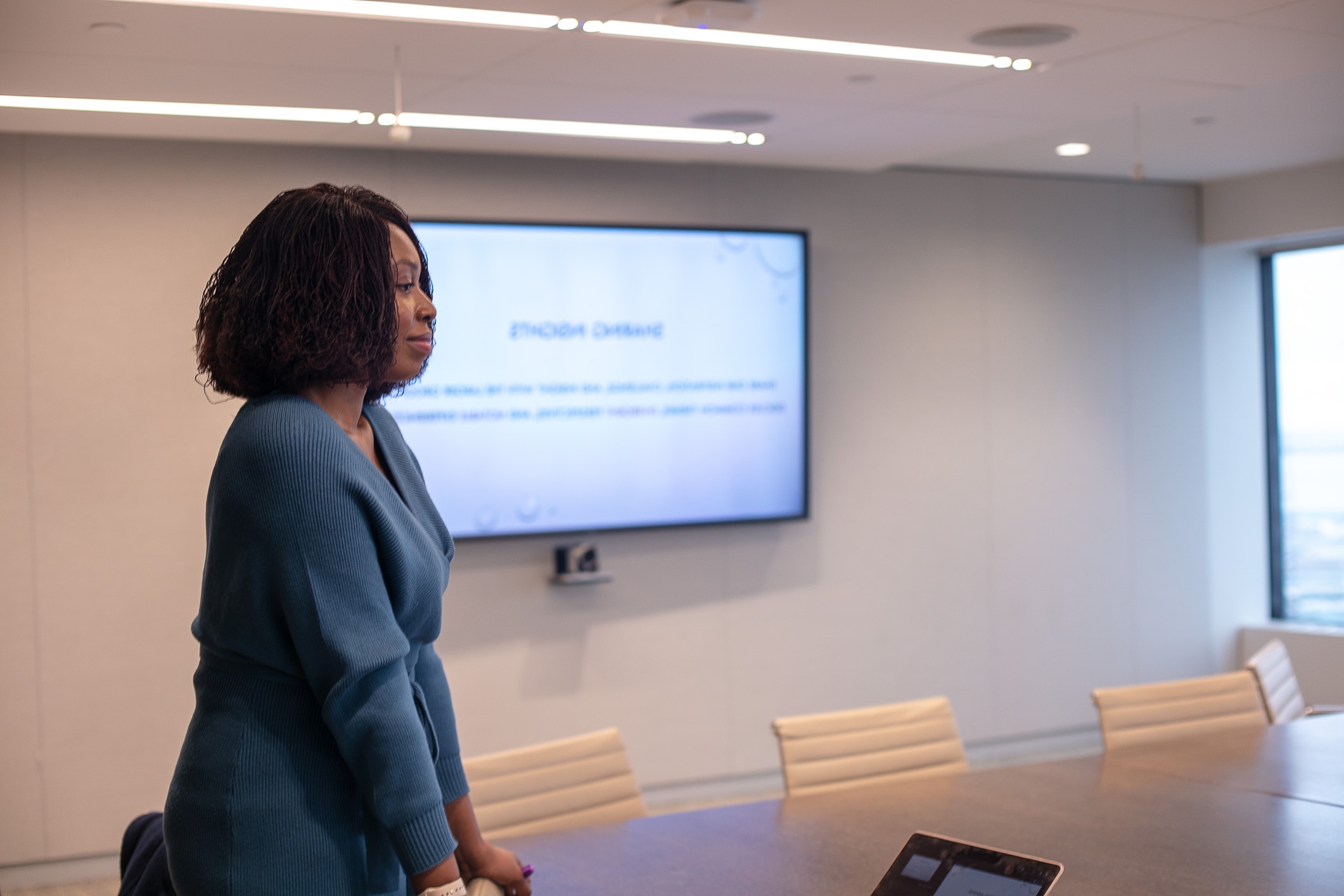 A black woman in a blue dress making a presentation in a conference room